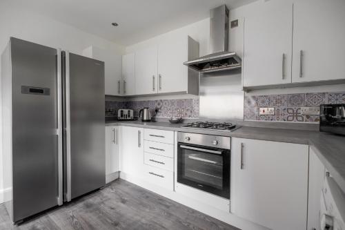 a kitchen with white cabinets and a stainless steel refrigerator at Grange House by Horizon Stays in Hartlepool