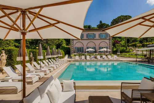 uma piscina com espreguiçadeiras brancas e guarda-sóis em Villa Cora em Florença