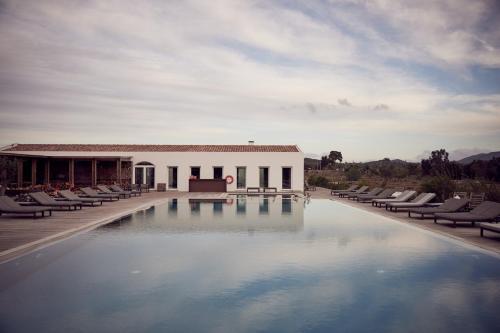 a swimming pool with chairs and a building at Craveiral Farmhouse by Belong Staying & Feeling in São Teotónio