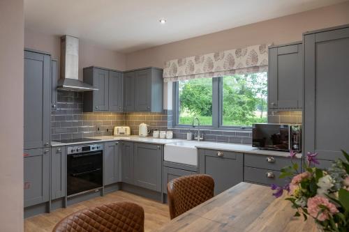 cocina con armarios grises y mesa de madera en Slatehouse Cottage, Drumlanrig en Thornhill