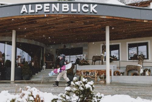a woman walking in front of a store holding a snowboard at Superior Sport und Familienresort Alpenblick in Zell am See