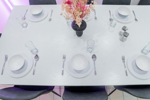 una mesa blanca con platos y cubiertos y un jarrón de flores en Berloga Capsule JBR, en Dubái