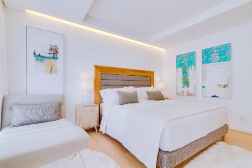 a white bedroom with a large bed and a chair at Pine Cliffs Village in Albufeira