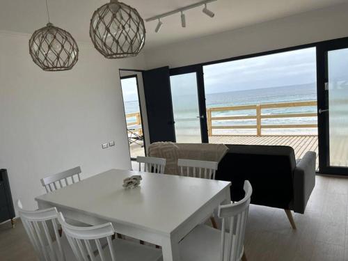 a dining room with a white table and chairs and the ocean at Cuatro Islas Lodge del Mar Cabaña Isla Damas in Choros
