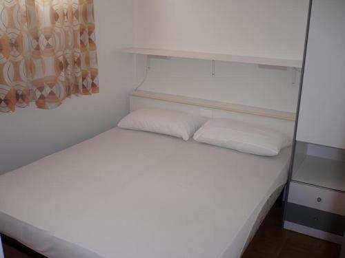 uma pequena cama branca com duas almofadas em Apartment Renata 26 em Lido di Jesolo