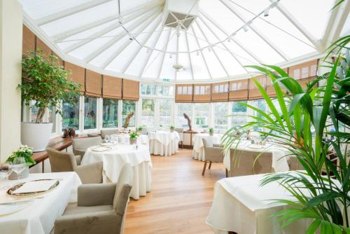 un restaurant avec des tables blanches, des chaises et des plantes dans l'établissement Le Manoir aux Quat'Saisons, A Belmond Hotel, Oxfordshire, à Great Milton