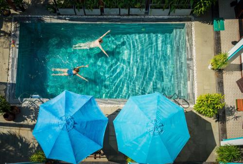 two people swimming in a swimming pool with blue umbrellas at Seagull Nest Hoi An Beach Village in Tân Thành (1)