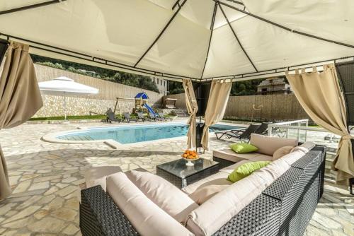 un patio con sofá y sombrilla junto a la piscina en 6 bedrooms villa with sea view private pool and jacuzzi at Dubravka Konavle en Dubravka