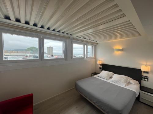 1 dormitorio con 1 cama y 2 ventanas en Hotel Punta Monpas en San Sebastián
