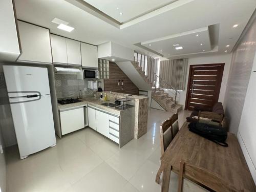 cocina con armarios blancos, mesa y nevera en Apartamento Porto Villa dos Diamantes 22 en Porto Seguro