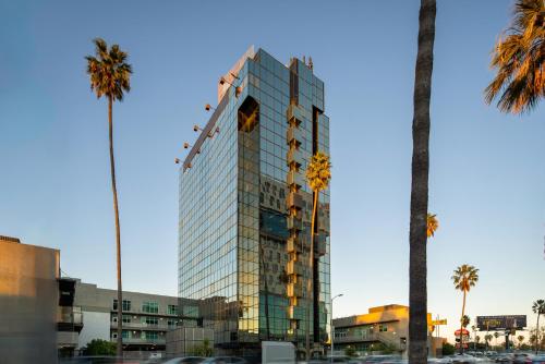 un grand bâtiment en verre avec des palmiers devant lui dans l'établissement Kasa Sunset Los Angeles, à Los Angeles
