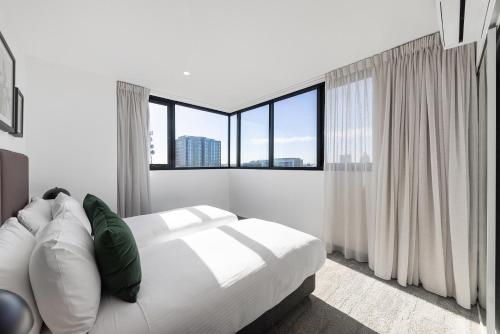 a white bedroom with a bed and large windows at Quest Geelong Central in Geelong