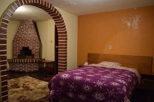 - une chambre avec un lit violet et un mur en briques dans l'établissement La Quiteñita Papallacta, à Papallacta