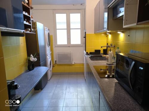 une grande cuisine avec des murs jaunes et une fenêtre dans l'établissement Aramis Colibri 72m2, lit king-size, baignoire duo hôte non professionnel, à Paris