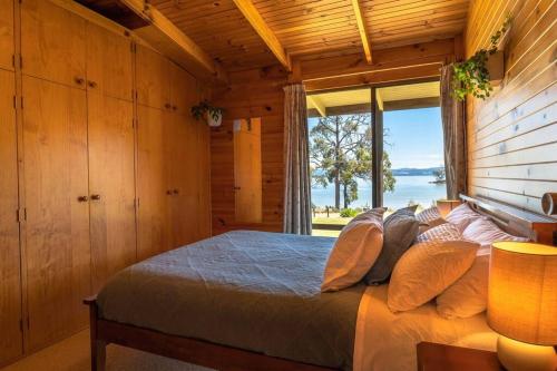 sypialnia z łóżkiem i dużym oknem w obiekcie The Cabin By the Sea - Cosy Waterfront Getaway w mieście Lunawanna