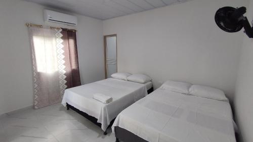 two beds in a white room with a window at Hostal torres del caribe in San Bernardo del Viento