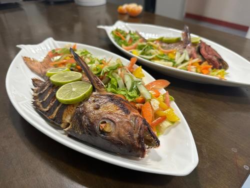 two plates of food with a fish and vegetables on a table at Blue Water Thoddoo Inn in Thoddoo