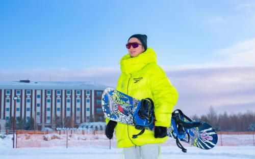 Ein Mann in einer gelben Jacke mit einem Snowboard. in der Unterkunft Rixos Borovoe in Borovoye
