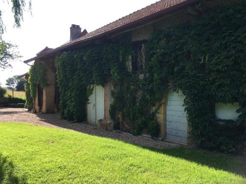 Semur-en-Brionnais的住宿－Les Granges De Semur-en-brionnais With Heated Poo，常春藤覆盖的房子,有白色的门和院子
