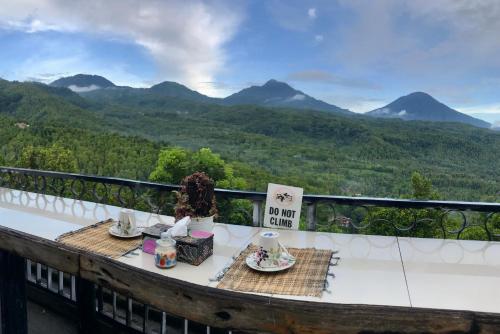 a table with plates of food on a balcony with mountains at Umah De Madya & Rooftop De Madya in Munduk