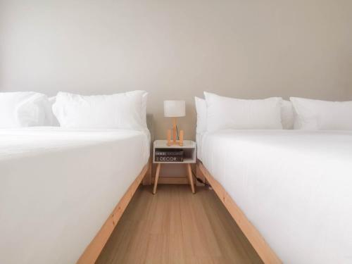 two beds with white sheets and a table with a lamp at D' Sara Sentral Suites by Manhattan Group in Sungai Buluh