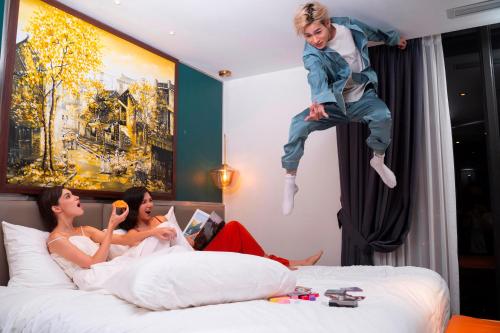 two women and a child jumping on a bed at Aurora Premium - A Lifestyle Hotel in Hanoi