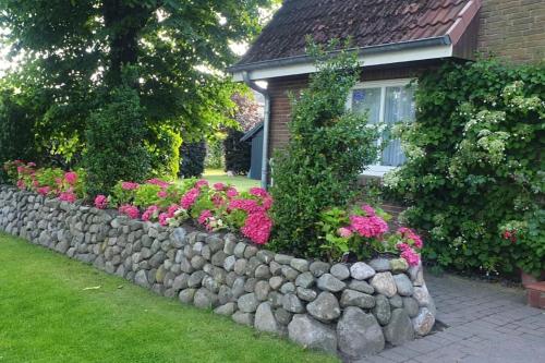 a stone retaining wall in front of a house with flowers at Whg Liesa, Heidweg 6 Nieblum in Nieblum