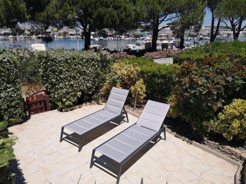 2 chaises longues assises sur une terrasse près de l'eau dans l'établissement APPARTEMENT 1 CHAMBRE 4 PERSONNES EN REZ DE CHAUSSEE DANS RESIDENCE AVEC PISCINE, au Grau-du-Roi