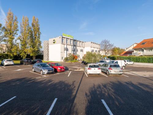 un parking avec des voitures garées devant un hôtel dans l'établissement B&B HOTEL Lyon Eurexpo Bron, à Bron