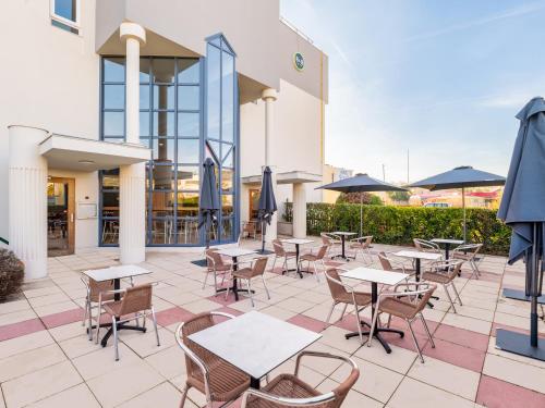 Un patio al aire libre con mesas, sillas y sombrillas. en B&B HOTEL Lyon Eurexpo Bron, en Bron
