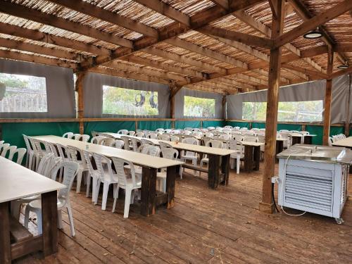 ein leeres Esszimmer mit Tischen und weißen Stühlen in der Unterkunft חאן דרך העץ - אוהל ממוזג וקמפינג in Shadmot Devora