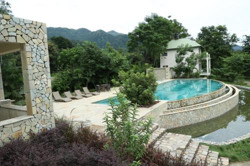 a swimming pool with a stone wall next to a house at The Corbett Greens in Rāmnagar