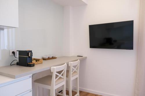 a kitchen with a counter with two stools and a television on a wall at Keys of Sicily - Residence "Sabbia" sul mare in Marina di Modica