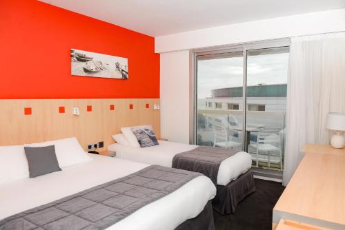 2 letti in una camera d'albergo con pareti arancioni di Kyriad Prestige Les Sables d'Olonne - Plage - Centre des Congrès a Les Sables-dʼOlonne