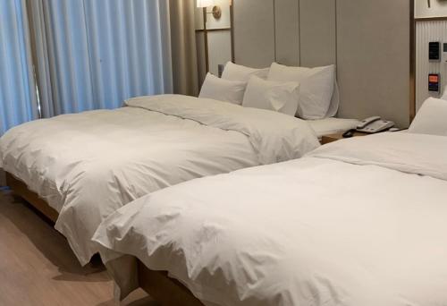 two beds with white sheets in a hotel room at H avenue Kijang Ilgwang in Busan
