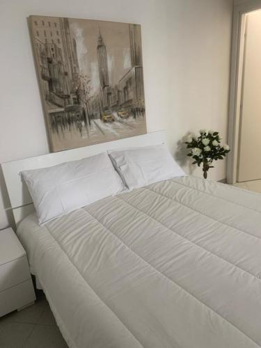 a white bed in a bedroom with a painting on the wall at La casa di Gio' in Fiumicino