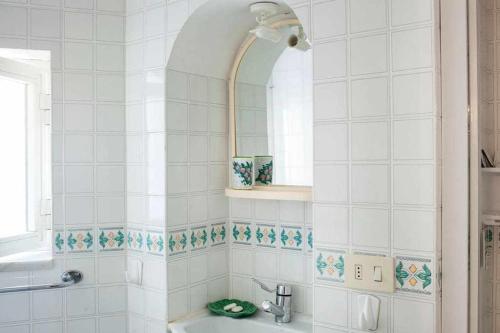een wit betegelde badkamer met een wastafel en een spiegel bij Donna Sara Appartamento in corte Amalfitana in Amalfi