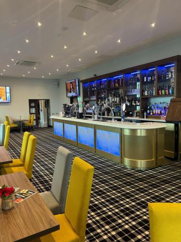 a bar in a restaurant with yellow chairs and tables at The Grand Hotel in Port Talbot