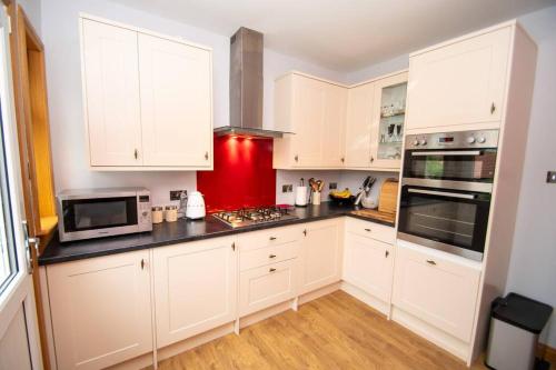 a kitchen with white cabinets and a red wall at Linburn Cottage Dunfermline near Edinburgh in Dunfermline