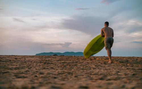 a man walking on the beach with a surfboard at Mad Monkey Hostel Nacpan Beach in El Nido