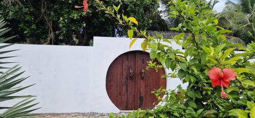 a wooden door in a white wall with a red flower at La VILLA BORAHA 300m2 PROPRIÉTÉ ENTIERE en bord de plage PISCINE PRIVEE Cuisine TV Wifi in Sainte Marie
