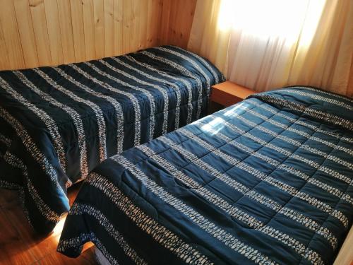 two beds in a room with a blue comforter at Cabañas Los Canelos Hermosa granja en Pucón in Pucón