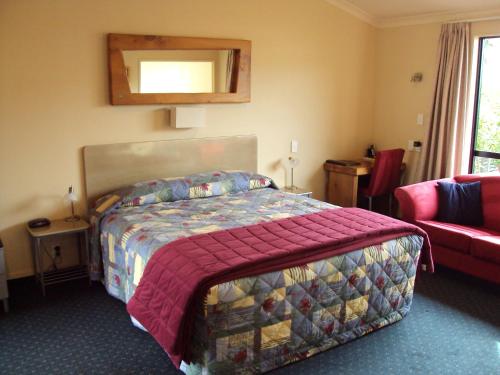 ein Schlafzimmer mit einem Bett und einem roten Sofa in der Unterkunft At The Rocks Motorlodge in Napier