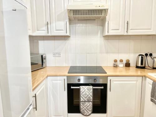 a kitchen with white cabinets and a stove top oven at Cosy 1 Bed, Wembley in London