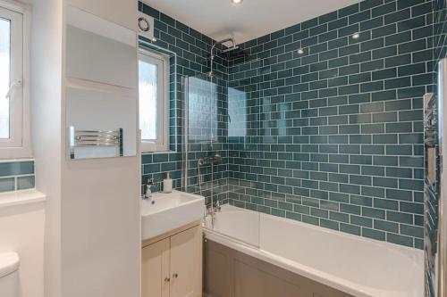 y baño con lavabo, bañera y azulejos verdes. en The Clissold, Two Bedroom Apartment N5, en Londres