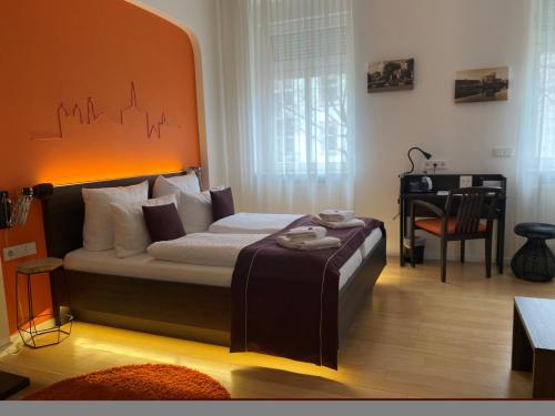 a bedroom with a bed with an orange headboard and a desk at sevenDays Hotel Karlsruhe in Karlsruhe