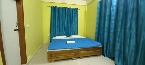 uma pequena cama num quarto com cortinas azuis em Kaziranga Balaji homestay em Kaziranga