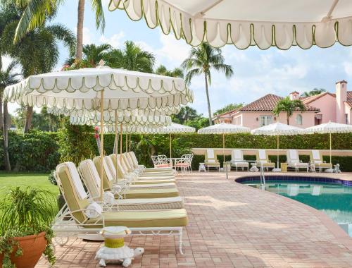 un grupo de sillas y sombrillas junto a una piscina en The Colony Hotel en Palm Beach