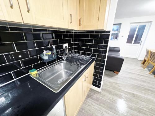 a kitchen with a sink and a black tiled wall at 2 Bedroom Tudor House Pristine and Comfortable Close to Birmingham City Hospital in Birmingham