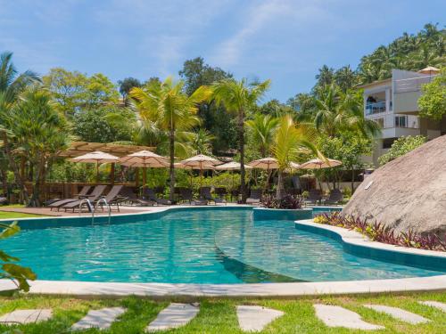 - une piscine dans un complexe avec des palmiers et des parasols dans l'établissement Velas do Engenho, à Ilhabela